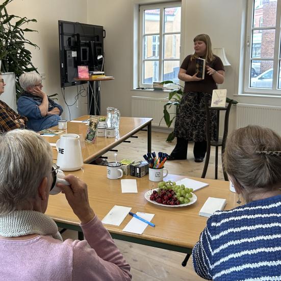 Mathilde holder en bog foran gæster til bogcafé