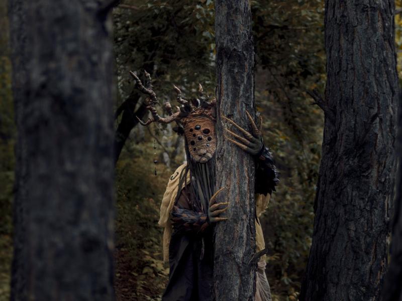 Uhyggelig maskeklædt træmand foran gammelt træ