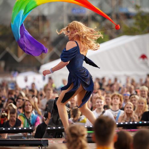 Dragperformer på scene svinger et stort regnbueflag foran en menneskemængde.