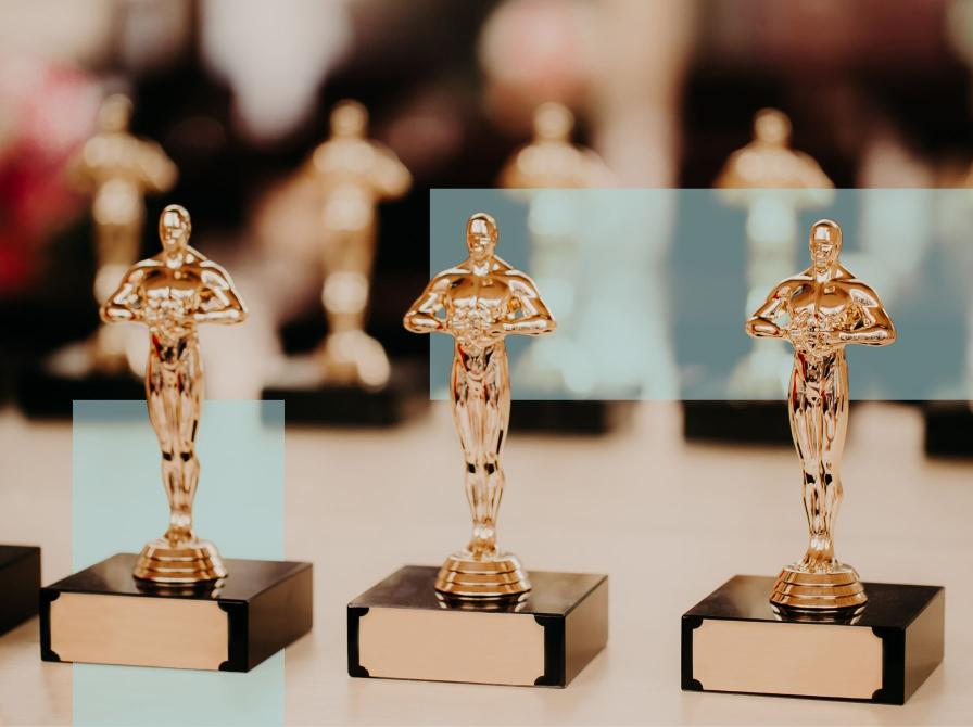 Tre prisstatuetter i forgrunden med flere lignende statuetter bagved.