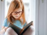 En rødhåret pige med briller, sidder på et bord og læser.