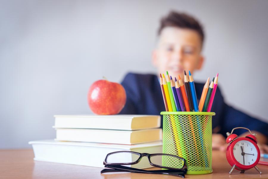 Stak af bøger i forskellige farver med et æble liggende ovenpå og en dreng i baggrunden.